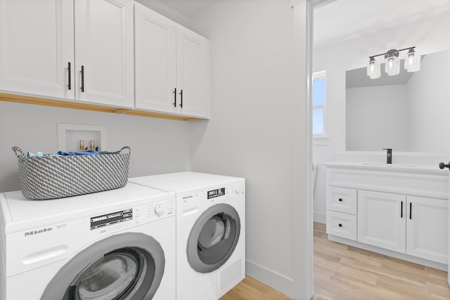 clothes washing area featuring cabinets, sink, washing machine and clothes dryer, and light hardwood / wood-style floors