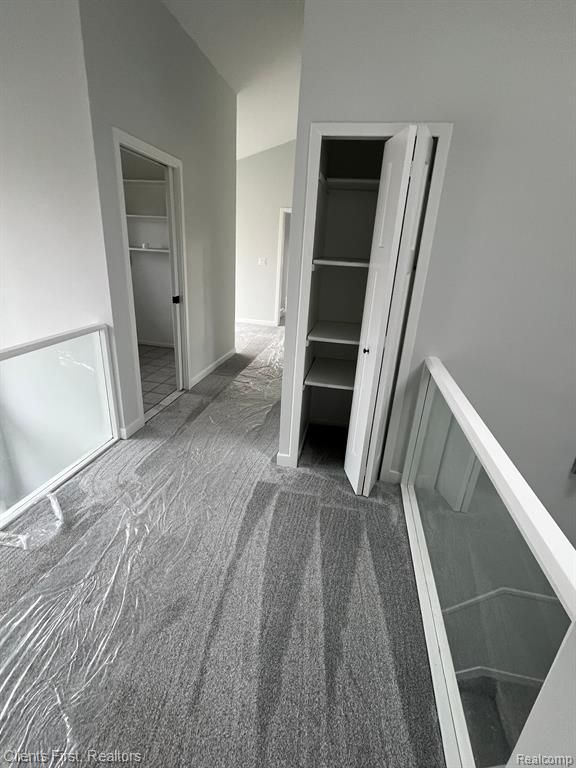 corridor featuring vaulted ceiling and dark colored carpet