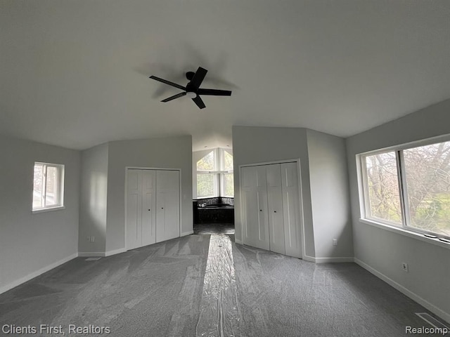 unfurnished bedroom with lofted ceiling, multiple windows, and multiple closets