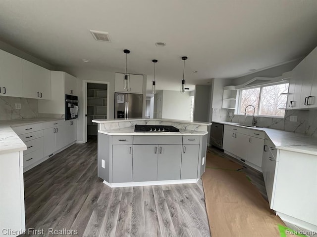 kitchen featuring a kitchen island, appliances with stainless steel finishes, decorative light fixtures, white cabinetry, and hardwood / wood-style flooring