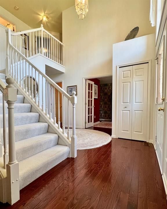 foyer entrance featuring dark wood-style floors, stairway, a towering ceiling, and baseboards