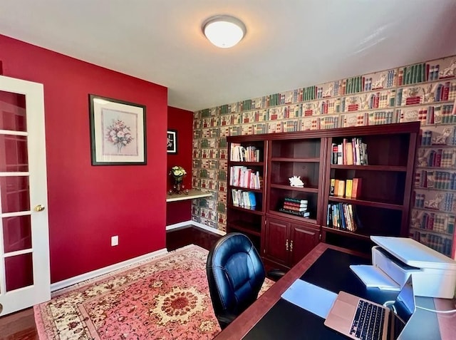 office area featuring wallpapered walls, an accent wall, baseboards, and wood finished floors