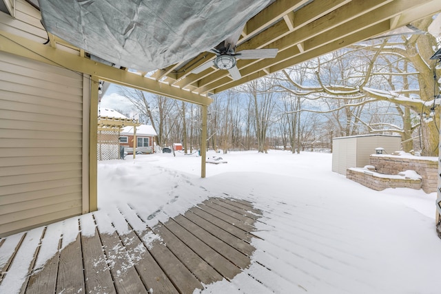 snow covered deck featuring ceiling fan, a shed, and a pergola