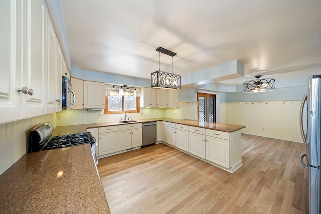 kitchen with light wood-type flooring, kitchen peninsula, decorative light fixtures, sink, and appliances with stainless steel finishes