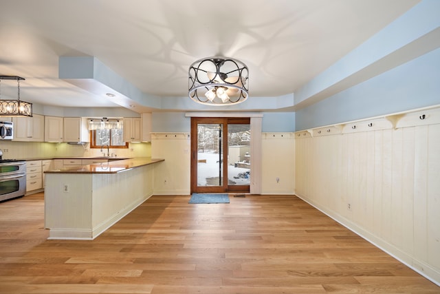 kitchen with light hardwood / wood-style flooring, a chandelier, sink, appliances with stainless steel finishes, and kitchen peninsula