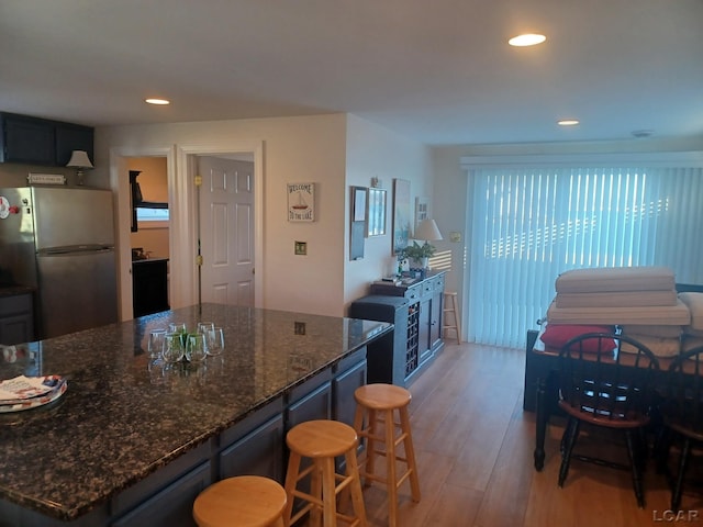 kitchen with stainless steel refrigerator, dark stone counters, and light hardwood / wood-style flooring