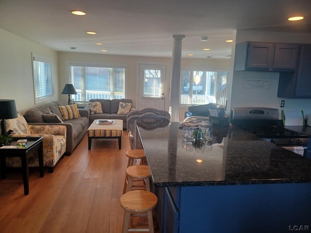 kitchen with light hardwood / wood-style flooring, a breakfast bar area, blue cabinets, gas range, and ornate columns