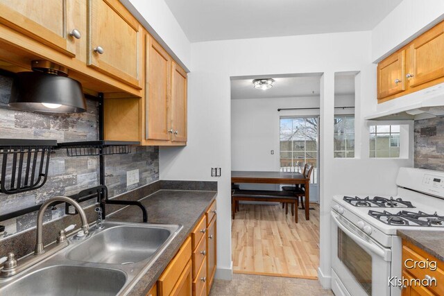 kitchen featuring white gas range oven, a sink, dark countertops, backsplash, and under cabinet range hood
