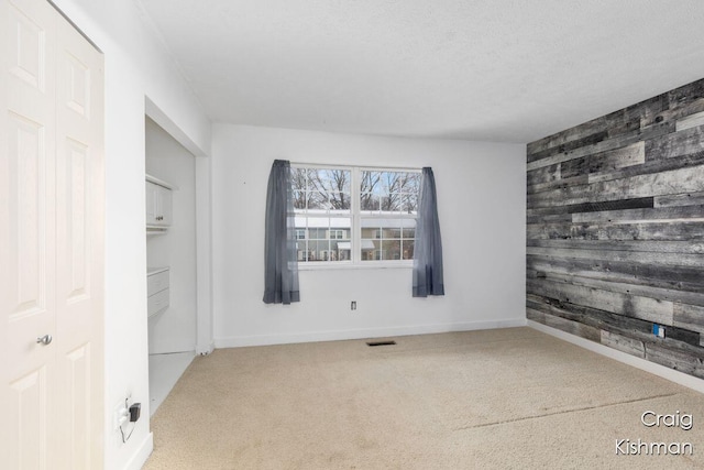 interior space with baseboards, visible vents, an accent wall, wooden walls, and carpet floors