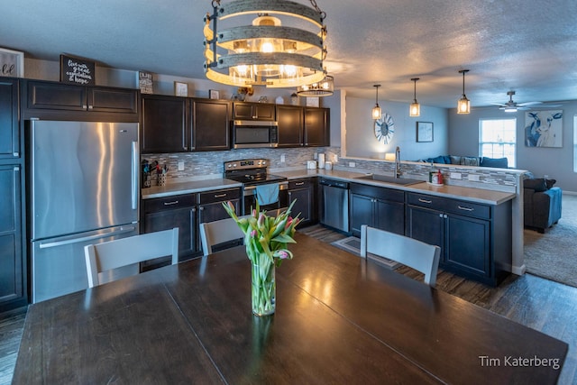 kitchen with sink, backsplash, stainless steel appliances, a textured ceiling, and decorative light fixtures