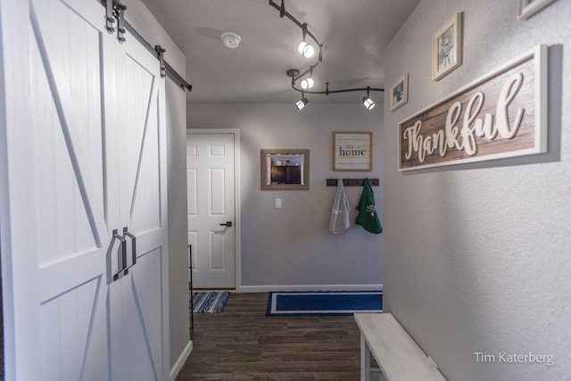 hallway with dark wood-type flooring, a barn door, and rail lighting