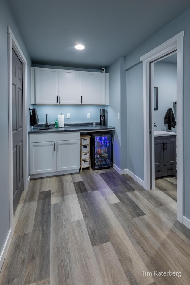 bar with white cabinetry, sink, beverage cooler, and light wood-type flooring