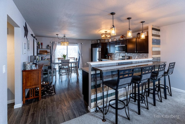 kitchen with a kitchen bar, hanging light fixtures, dark brown cabinetry, kitchen peninsula, and stainless steel appliances