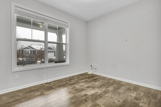 empty room featuring visible vents, dark wood finished floors, and baseboards