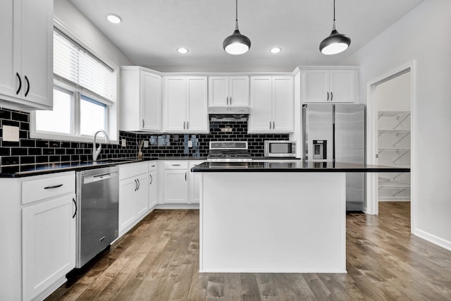 kitchen featuring pendant lighting, stainless steel appliances, dark countertops, white cabinetry, and a kitchen island