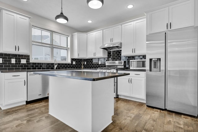 kitchen featuring dark countertops, hanging light fixtures, appliances with stainless steel finishes, white cabinetry, and under cabinet range hood