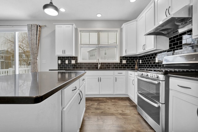 kitchen with range with two ovens, dark countertops, white cabinetry, a sink, and under cabinet range hood