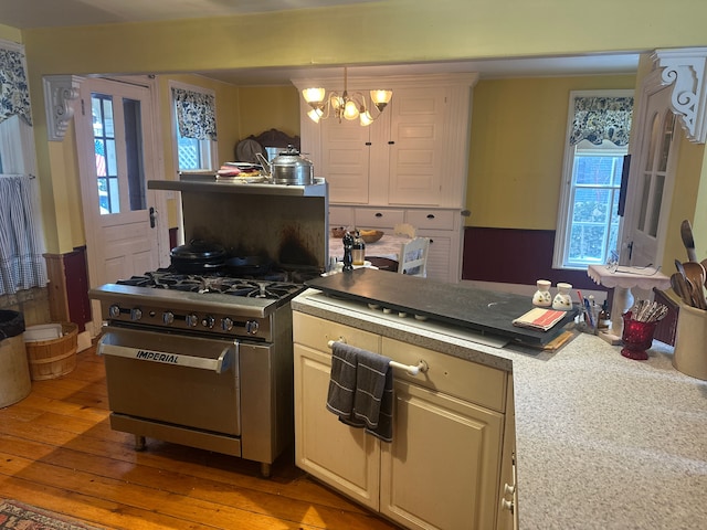 kitchen featuring high end range, hardwood / wood-style flooring, hanging light fixtures, a notable chandelier, and cream cabinets