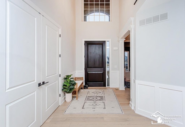 entryway featuring decorative columns, a high ceiling, and light wood-type flooring