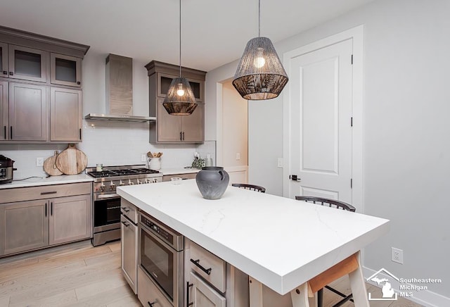 kitchen featuring a kitchen breakfast bar, a kitchen island, pendant lighting, stainless steel appliances, and wall chimney range hood