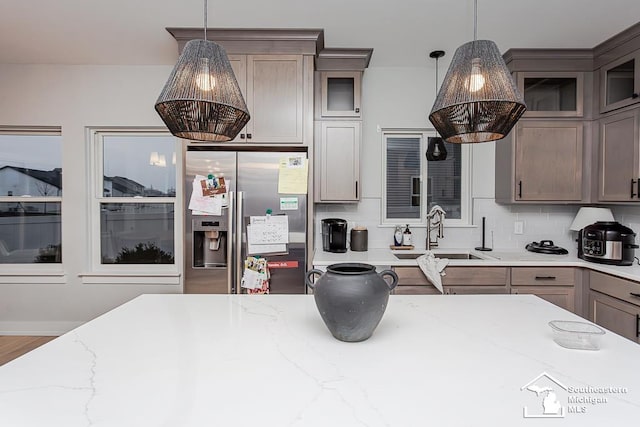 kitchen featuring sink, hanging light fixtures, backsplash, light stone counters, and stainless steel fridge with ice dispenser