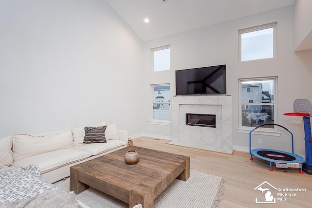 living room with plenty of natural light, light wood-type flooring, a fireplace, and high vaulted ceiling