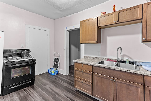 kitchen featuring dark hardwood / wood-style floors, sink, light stone countertops, and black gas range