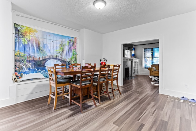 dining space with wood-type flooring, a brick fireplace, and a textured ceiling