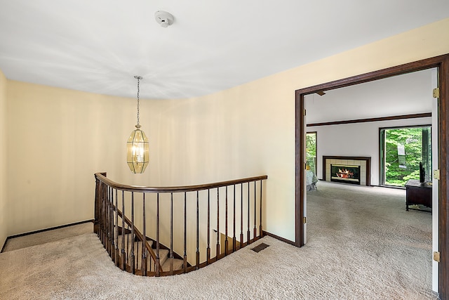 stairway featuring a tiled fireplace, carpet flooring, and an inviting chandelier