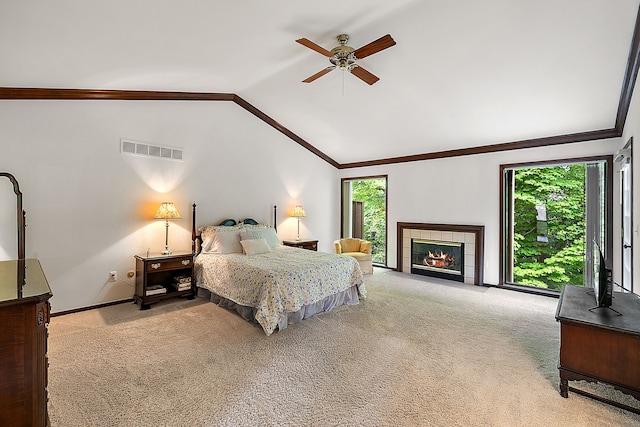 carpeted bedroom featuring a tiled fireplace, vaulted ceiling, ornamental molding, and ceiling fan