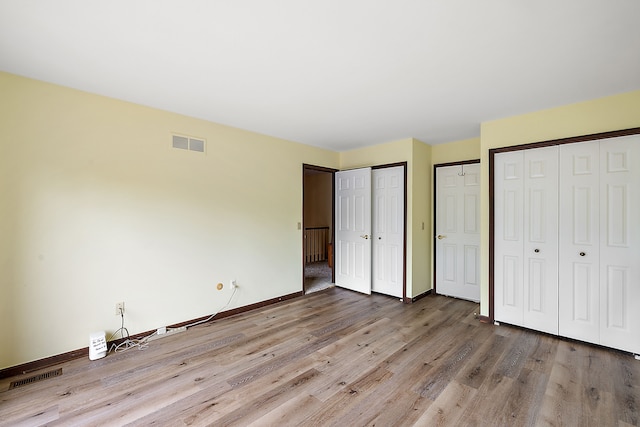 unfurnished bedroom with multiple closets and light wood-type flooring