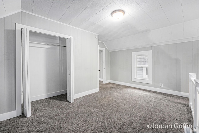 unfurnished bedroom with lofted ceiling, wooden walls, a closet, and dark colored carpet