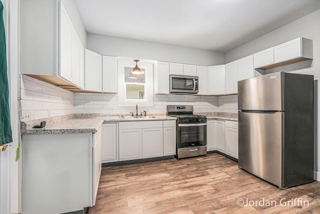 kitchen with sink, white cabinetry, appliances with stainless steel finishes, light hardwood / wood-style floors, and decorative backsplash