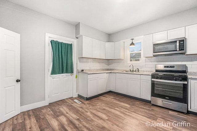 kitchen featuring sink, appliances with stainless steel finishes, backsplash, wood-type flooring, and white cabinets