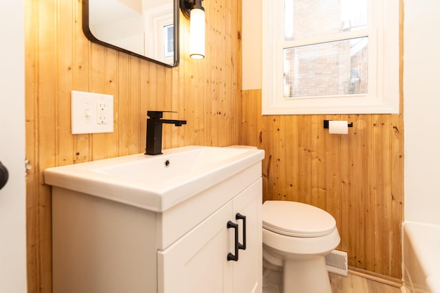 bathroom with vanity, wooden walls, and toilet