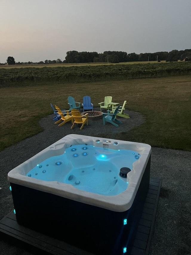 pool at dusk featuring a rural view, an outdoor hot tub, a yard, and an outdoor fire pit