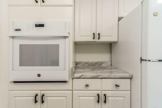 kitchen featuring white appliances, light stone countertops, and white cabinets