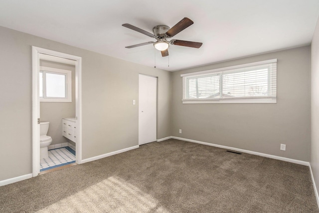 unfurnished bedroom featuring multiple windows, connected bathroom, and dark carpet