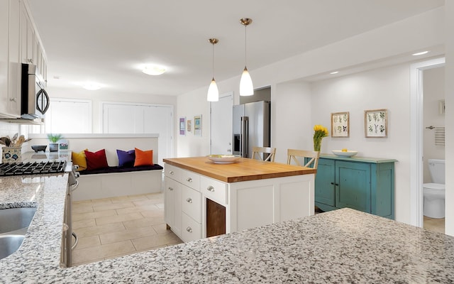 kitchen with pendant lighting, appliances with stainless steel finishes, white cabinets, light tile patterned flooring, and butcher block countertops