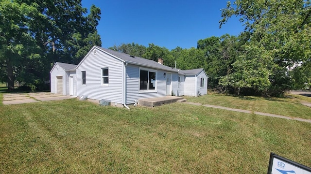930 W Barney Ave, Muskegon, MI 49441 - view of front of property with a front lawn, concrete driveway, a chimney, an attached garage, and an outbuilding