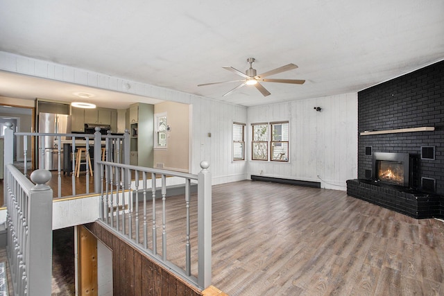 unfurnished living room featuring wood-type flooring, ceiling fan, a fireplace, and baseboard heating