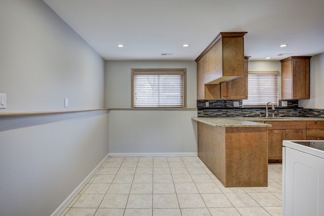 kitchen featuring light tile patterned flooring, a healthy amount of sunlight, kitchen peninsula, and light stone countertops