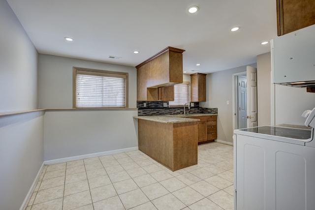 kitchen featuring light tile patterned flooring, washer / clothes dryer, sink, range, and kitchen peninsula