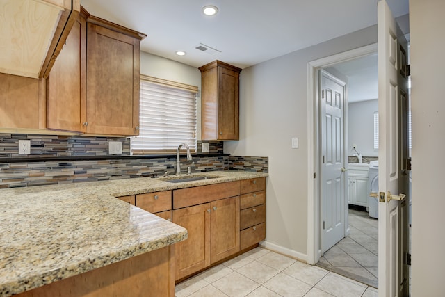 kitchen with sink, light tile patterned floors, backsplash, independent washer and dryer, and light stone counters