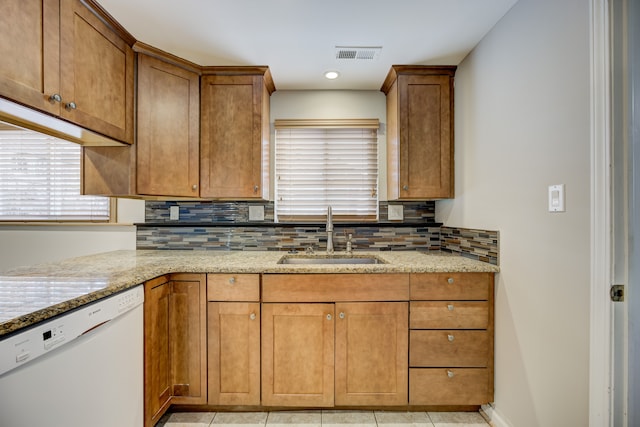 kitchen featuring dishwasher, sink, light stone counters, and decorative backsplash