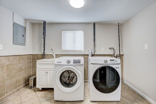 washroom featuring light tile patterned floors, tile walls, electric panel, cabinets, and separate washer and dryer