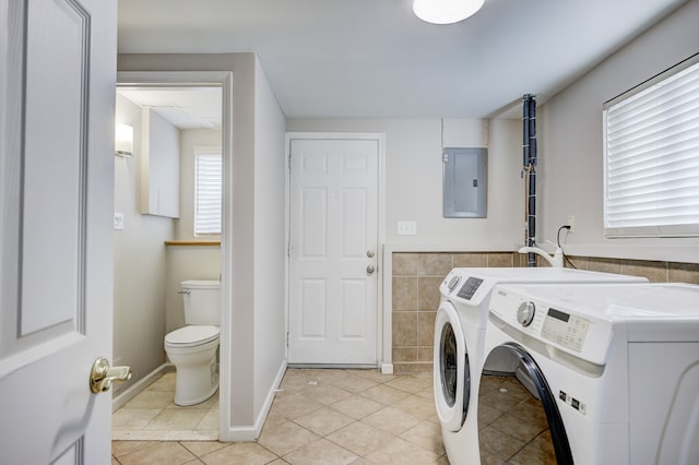 clothes washing area featuring independent washer and dryer, electric panel, tile walls, and light tile patterned floors