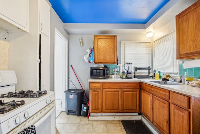 kitchen featuring white gas range, backsplash, sink, and light tile patterned flooring