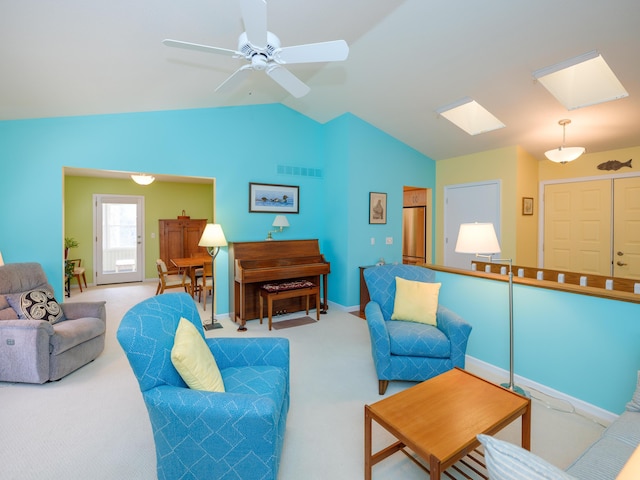 carpeted living room with ceiling fan and vaulted ceiling with skylight