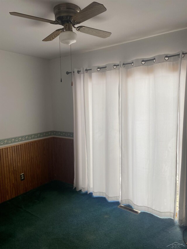 unfurnished room featuring ceiling fan, wooden walls, and carpet floors